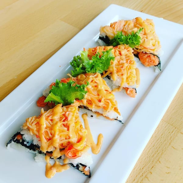 Four triangular sushi pieces topped with orange sauce and lettuce on a white rectangular plate.