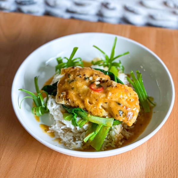 Curried fish with rice, bok choy, and green onions in a white bowl on a wooden table.