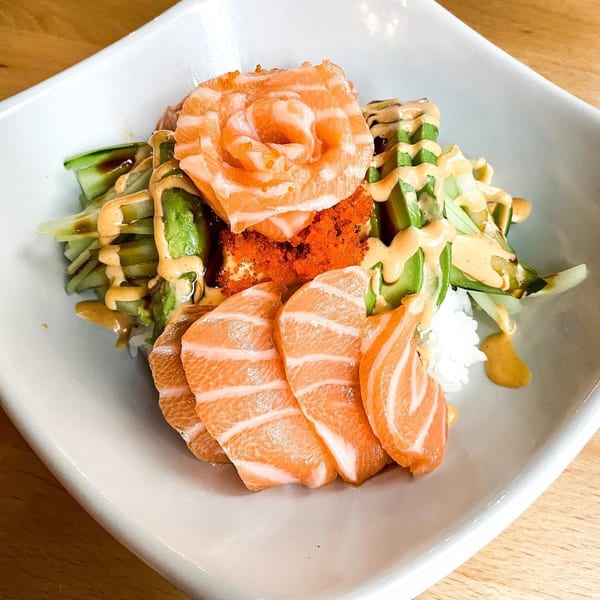 Salmon sashimi, roe, avocado, and cucumber salad with sauce in a white bowl.