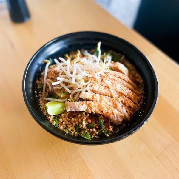 Black bowl of Pad Thai with sliced chicken, bean sprouts, crushed peanuts, and a lime wedge.