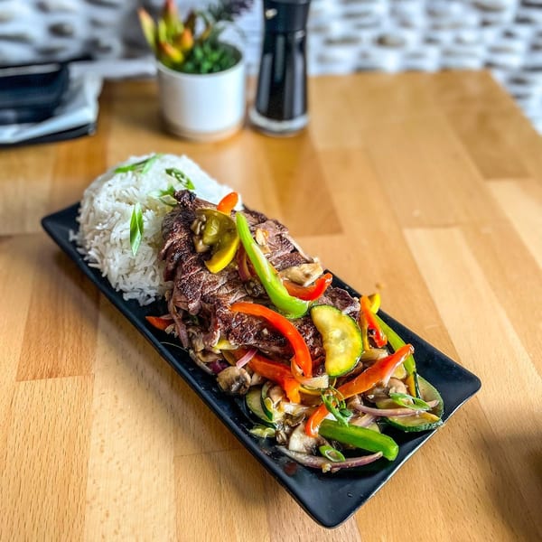 Grilled steak with colorful bell peppers, zucchini, and mushrooms, served with white rice.