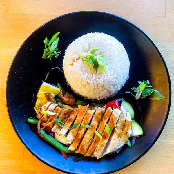 Grilled chicken with stir-fried vegetables and a mound of white rice on a black plate.