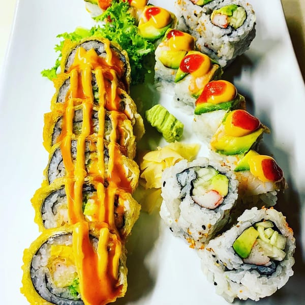 A white plate holds three types of sushi rolls, including tempura, California, and avocado-topped.